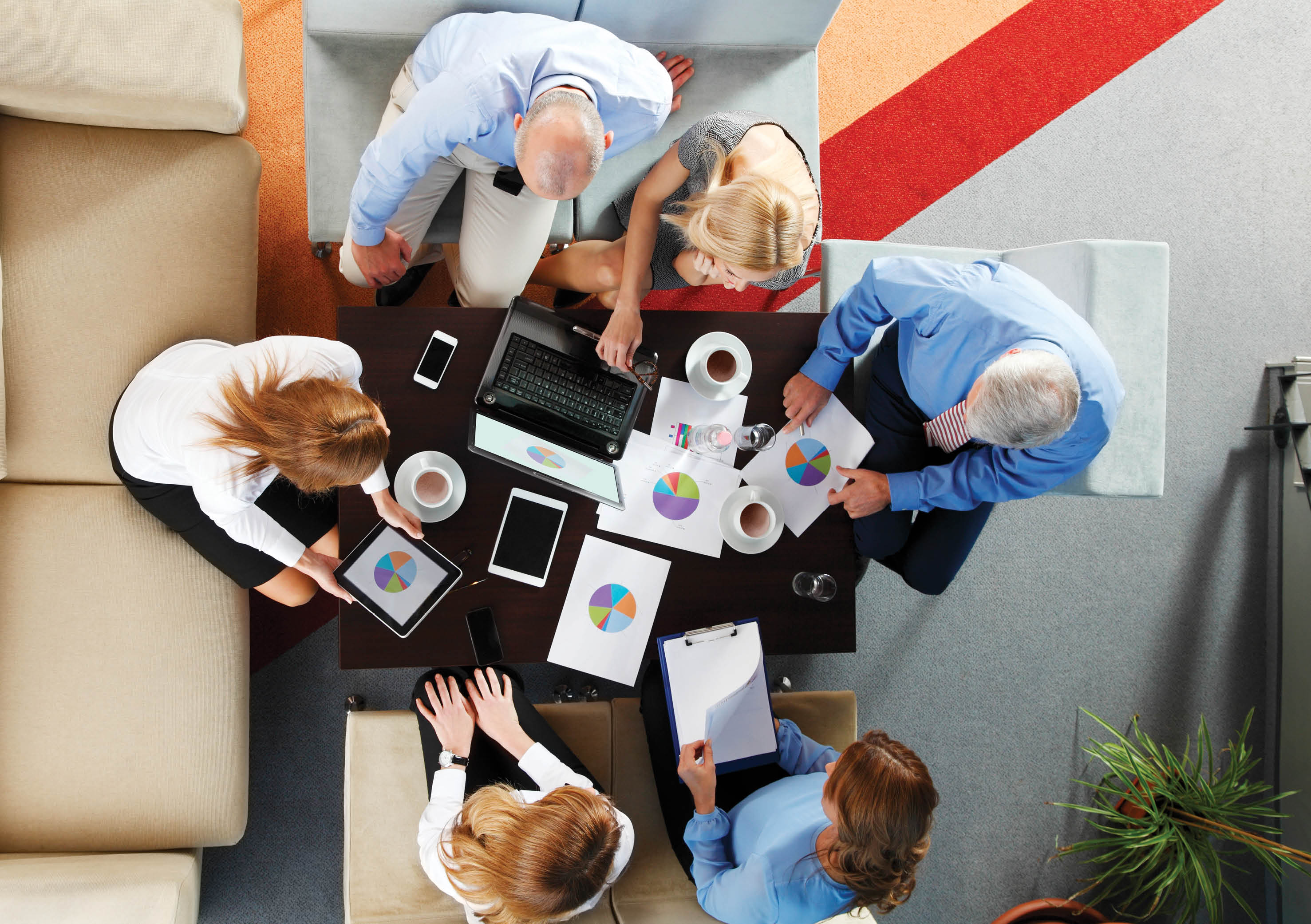High angle view of business team in a meeting. Businesswomen and businessmen sitting around conference table and working with laptop and digital tablet analyzing diagrams.