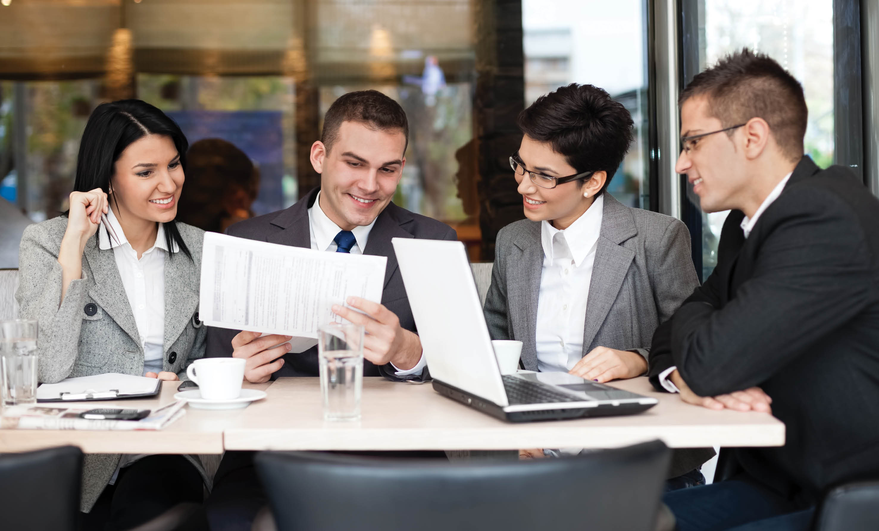  Group of four young business people gathered together at a table discussing an interesting idea in the cafe